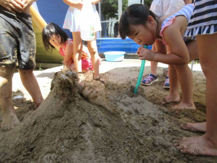 先生と数人の女の子でこっそり砂場に火山づくり。どうしたらみんなが驚いてくれるか考えながら、ホースを砂で埋めました。みんなで水遊びに園庭に出た時に砂場にみんなで集まってもらっていざ噴火!見てくれたお友だちも、作ったお友だちもみんなで驚いてどんどんお友だちが集まり大人気になりました。遊んでいくうちに「もっとみずいれてみたら?」などいろいろな工夫も出て楽しい遊びでした。