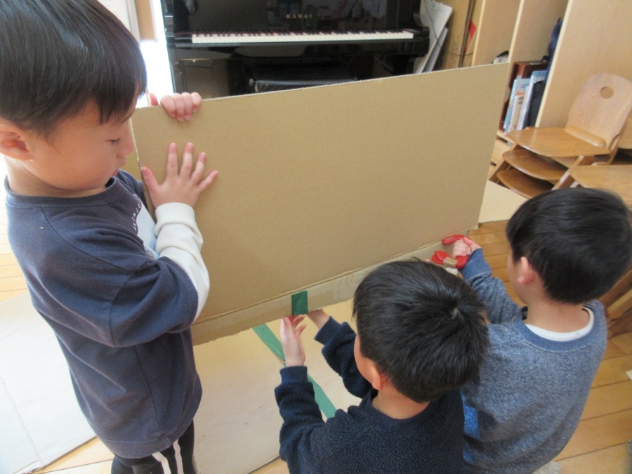 みんなで考えたお話の劇「かなへびのかなちゃん遠足大冒険の巻」の配役が決まると、「服、作らんなん」「お池もいる」と気づいて、早速衣装や大道具作りが始まりました。お友だちが段ボールカッターを使っていると、切りやすいように他のお友だちがすっと段ボールを持って、チームワークもバッチリなばら組さん。登園後にはリュックサックやお弁当など自分で必要と思ったものを自主的に作っているお友だちもいて、工夫しながら作ることを楽しんでいます。
